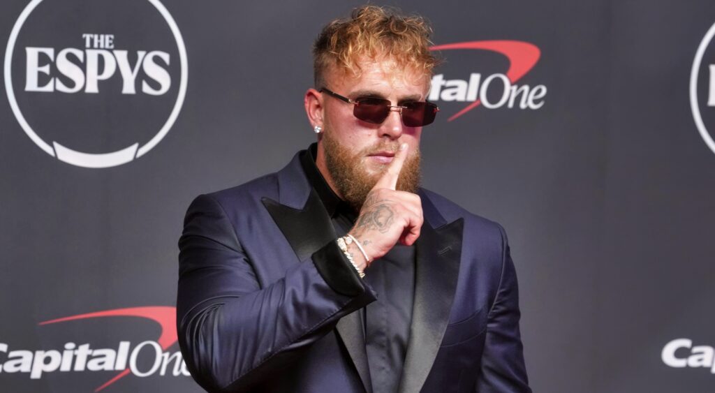Jake Paul in a suit with his finger by his mouth.